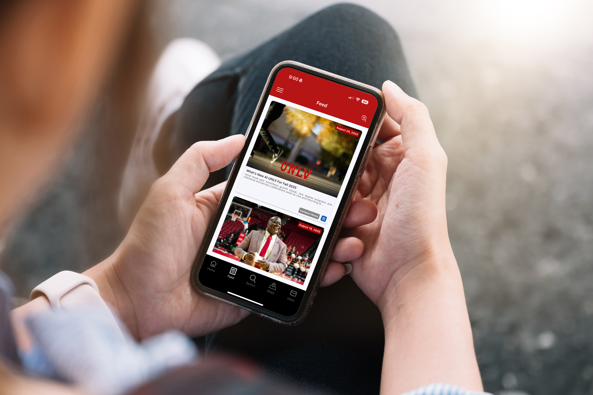 Person holding phone with UNLV Mobile app feed open. 