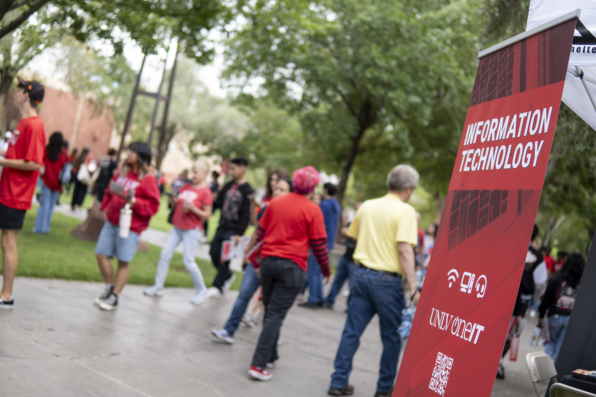 Groups of students walking past a red Information Technology banner. 