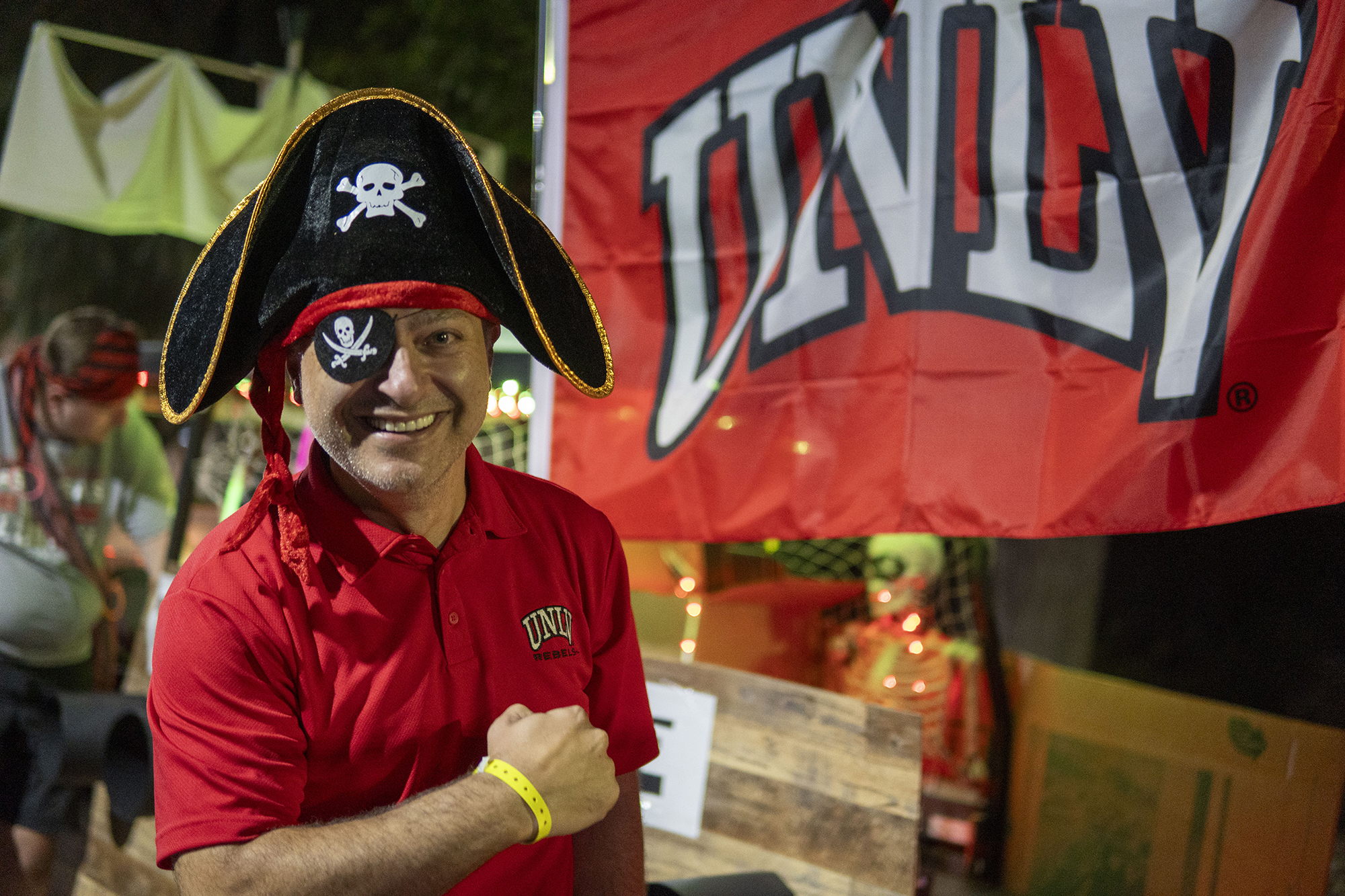 Person in red shirt with black pirate hand standing in front of red flag with white "UNLV" letters.