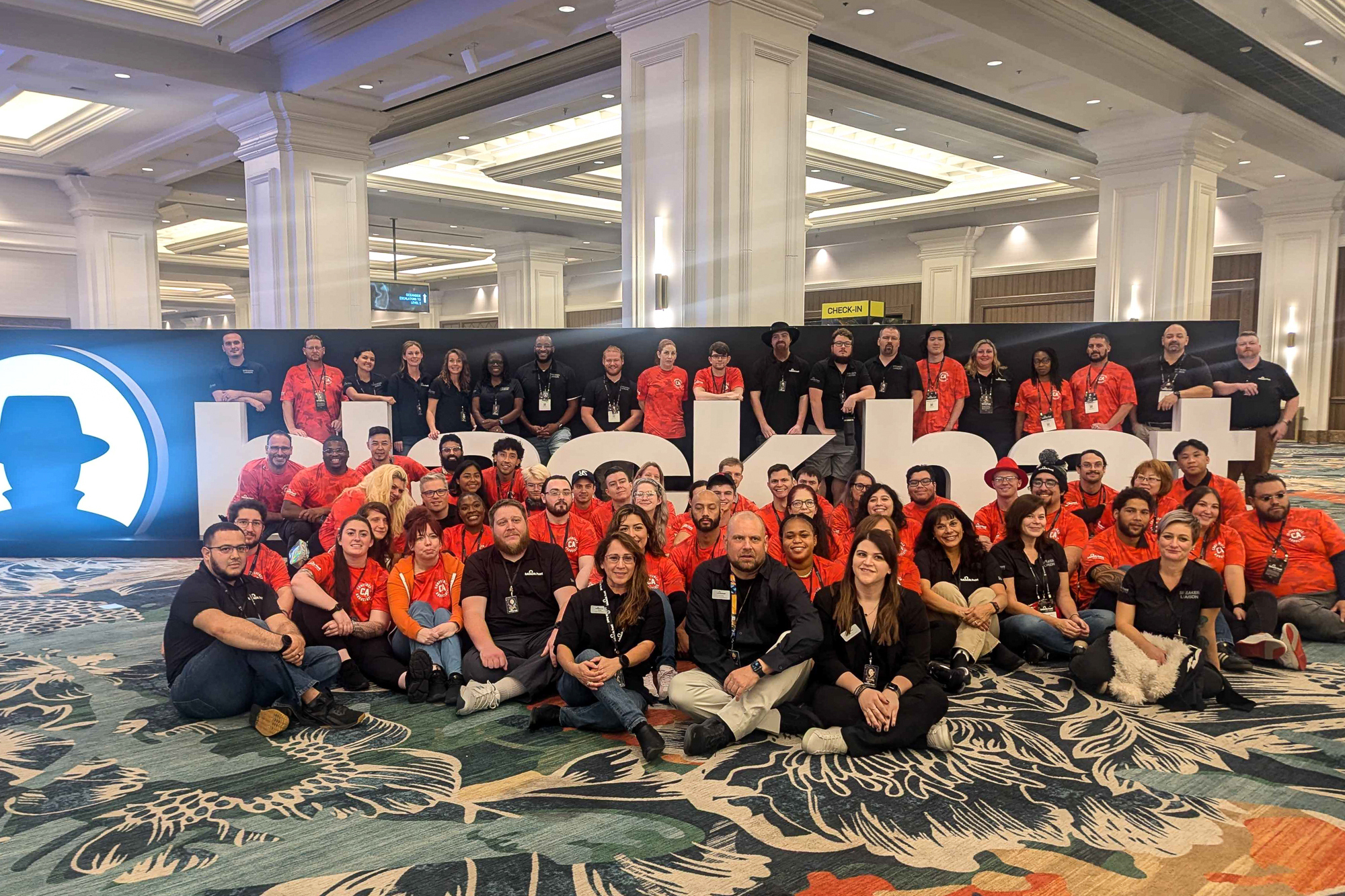 Group of people standing and sitting in front of white blackhat sign. 