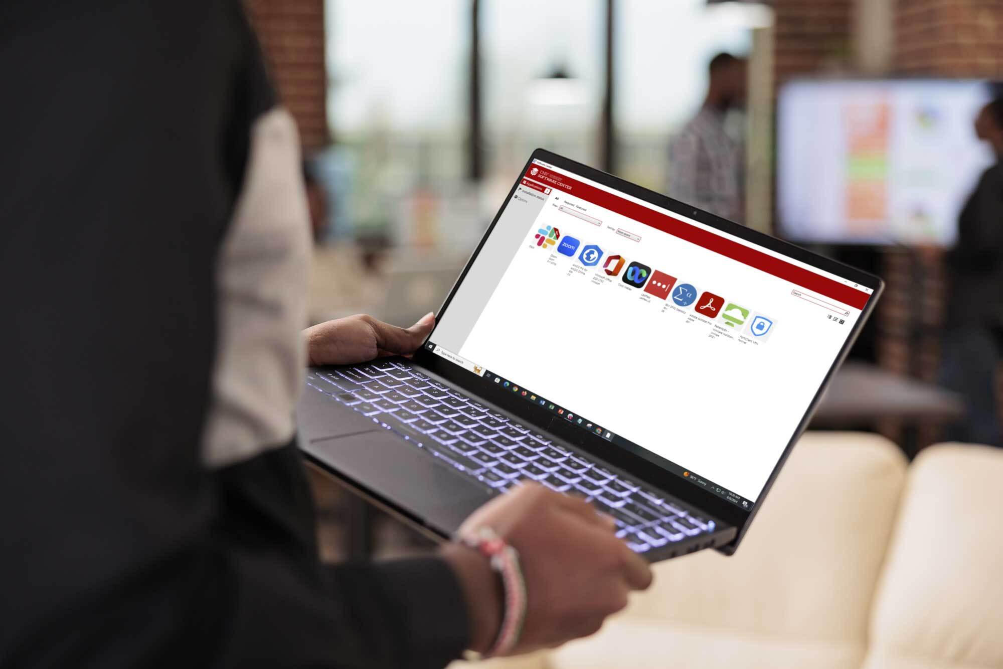 Person holding laptop with Software Center on screen.