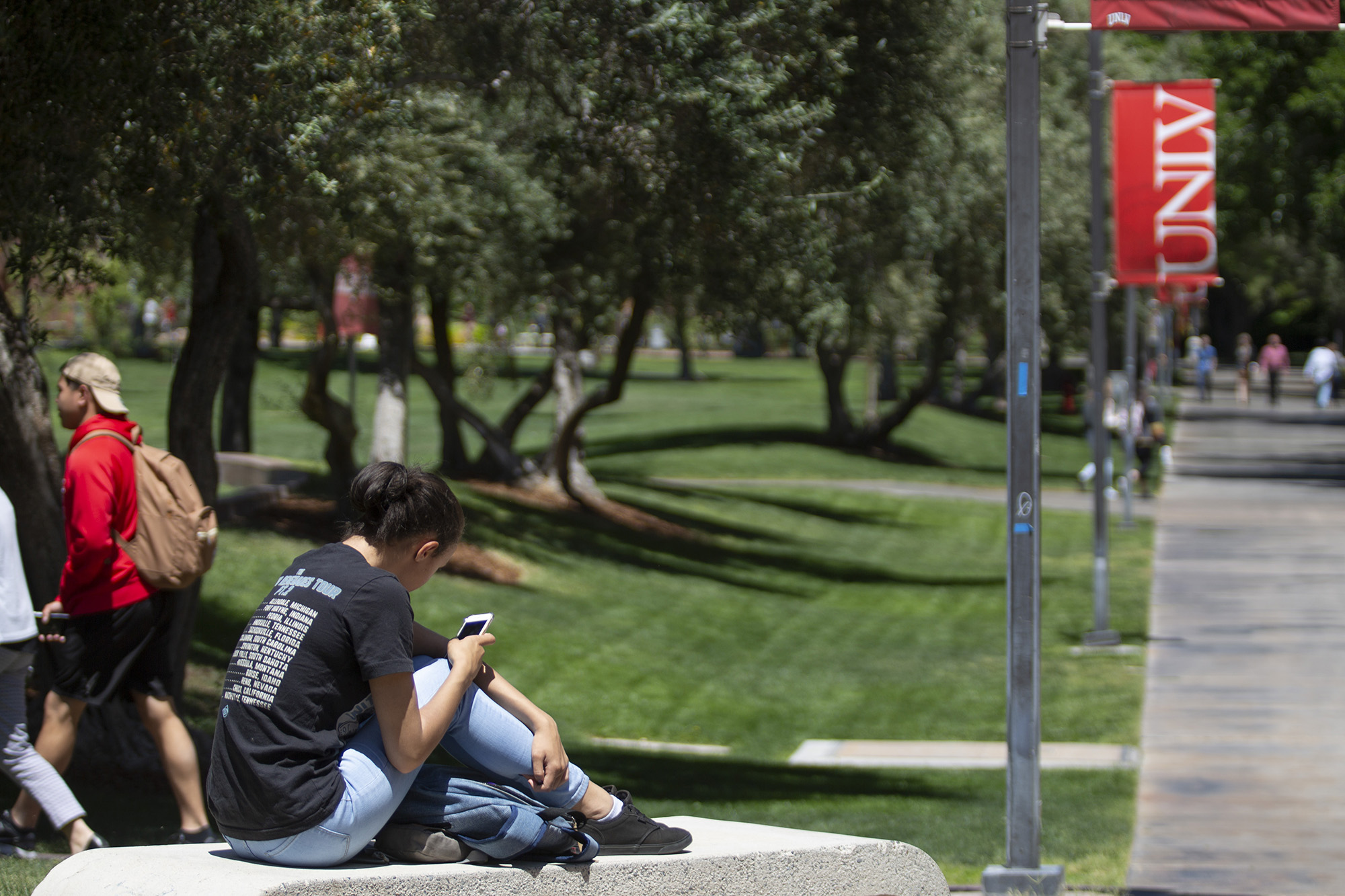 A female student sits near a red U-N-L-V banner looking at her mobile device.