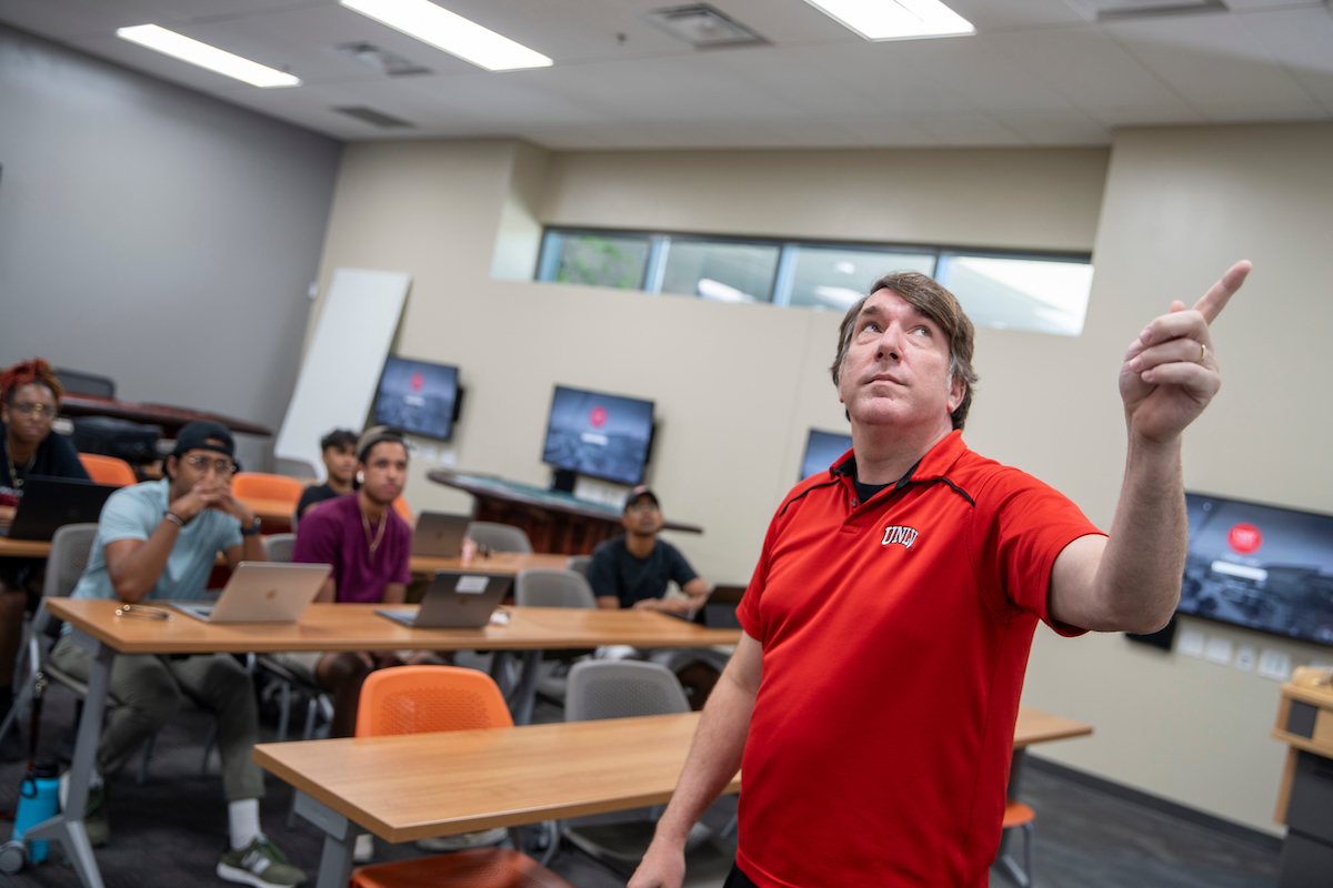 instructor pointing at the screen in front of students in a classroom