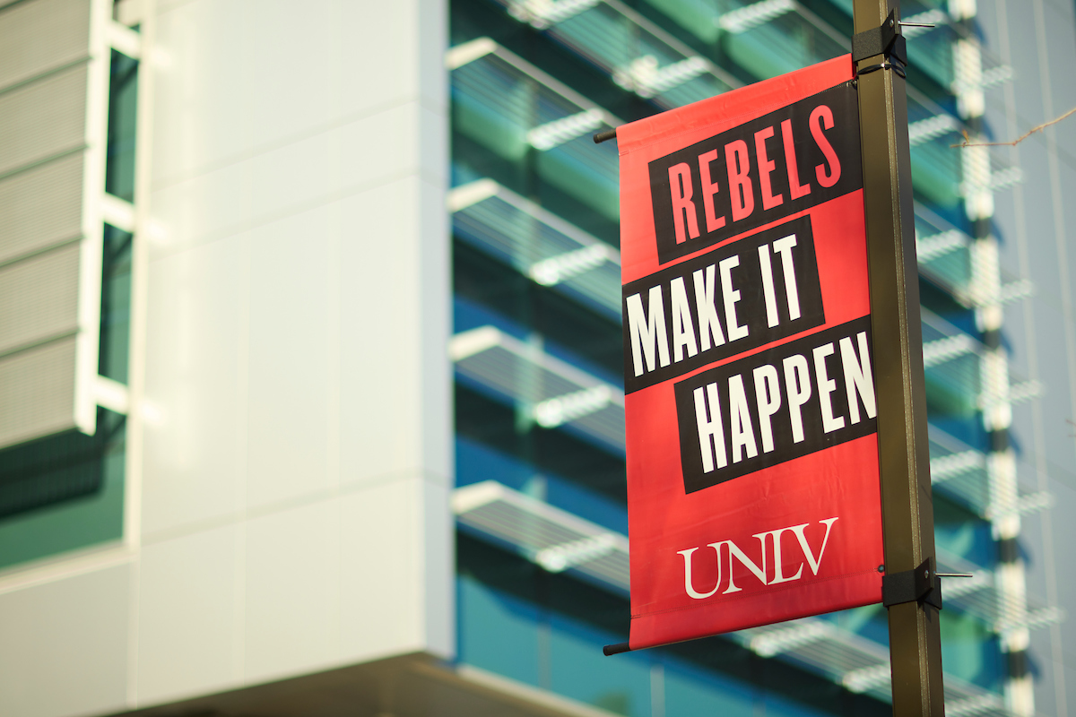 UNLV banner in front of the the Lied Library banner reads Rebels make it happen