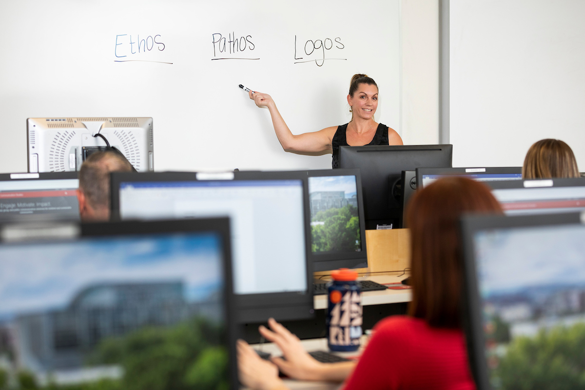 Instructor pointing at the whiteboard with students in the foreground using classroom computers