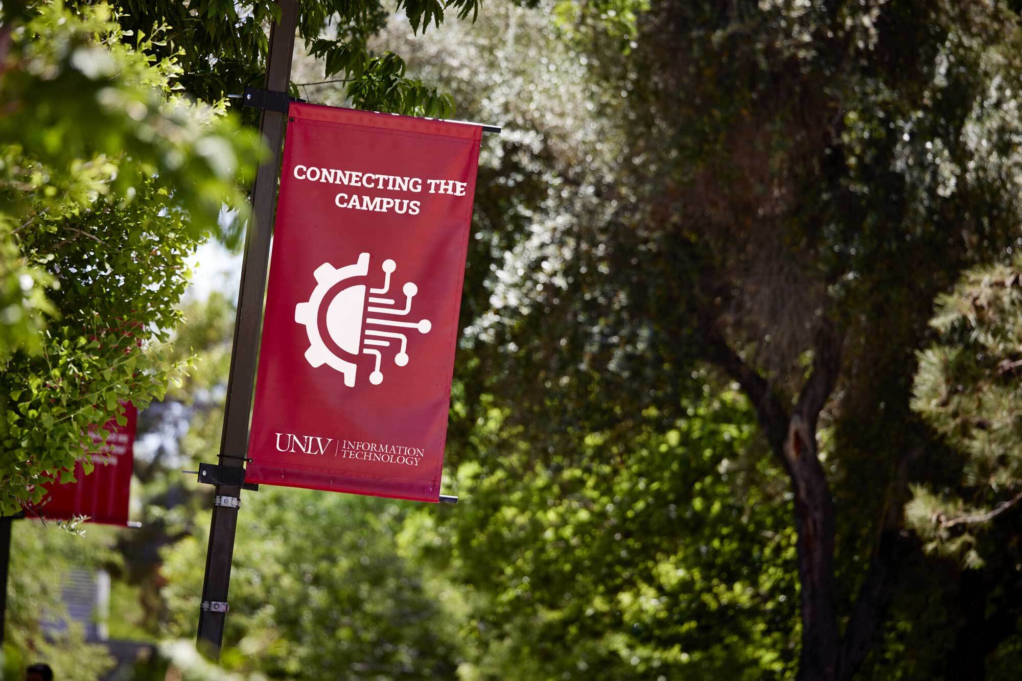 Close shot of a red UNLV IT connecting campus banner with a green foliage background.