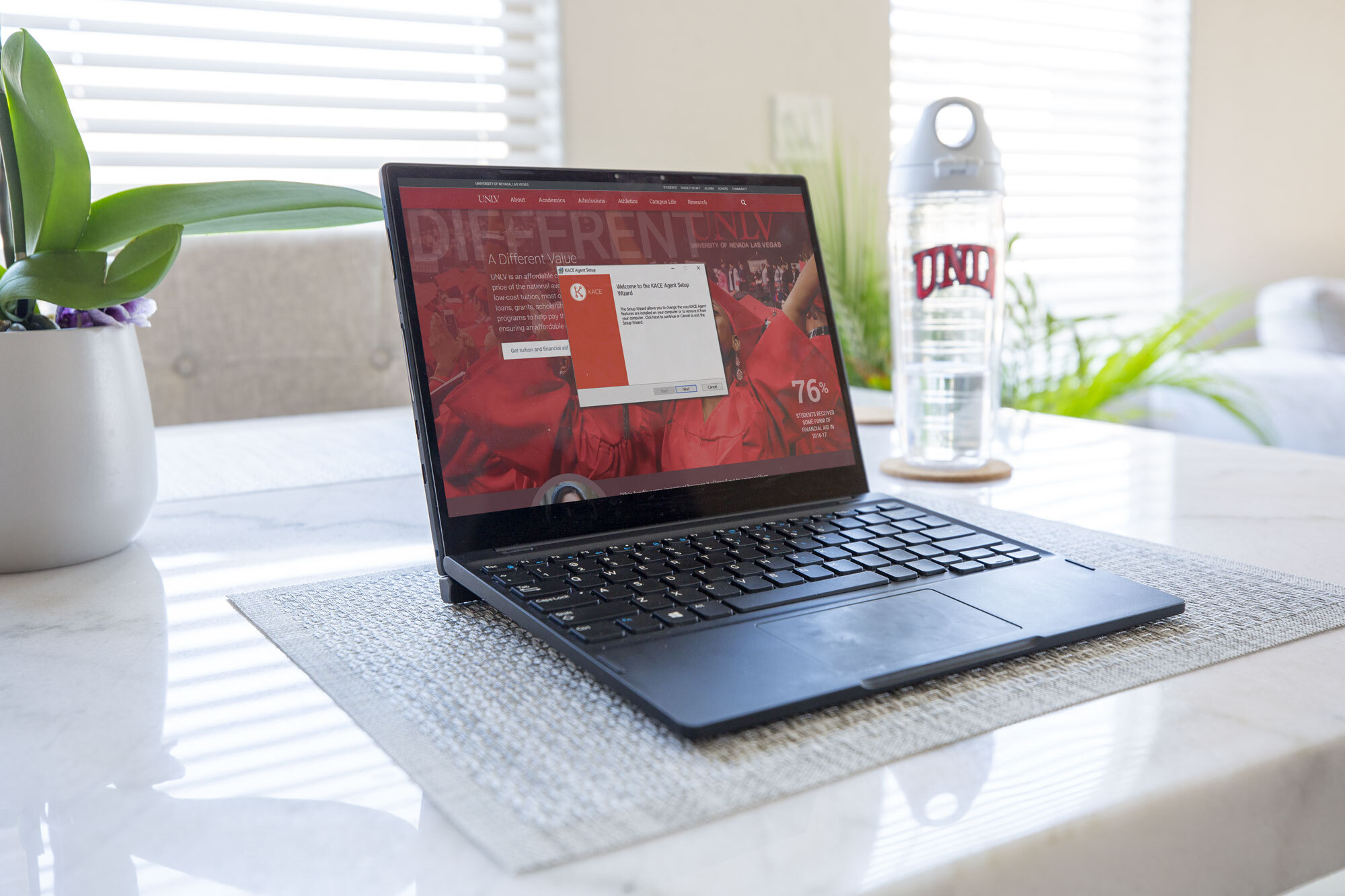 A laptop with the KACE agent setup wizard on the screen sits on a table.