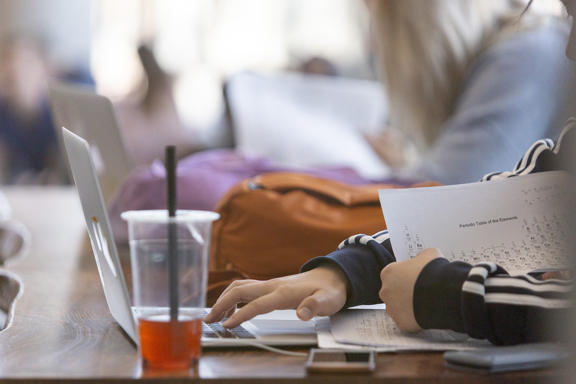 Close shot of one hand holding study papers while the other types on a laptop keyboard.