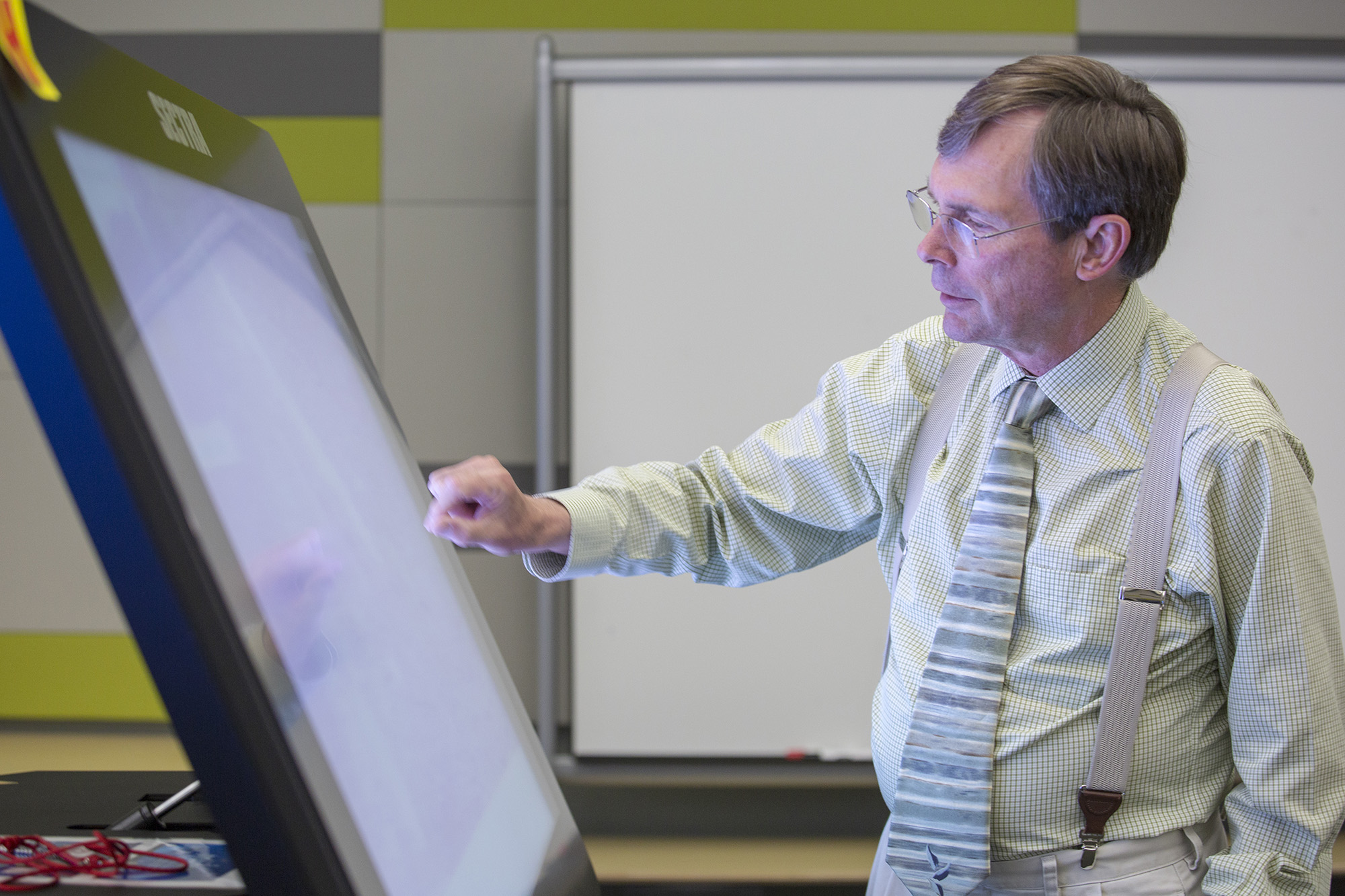 An instructor reaches a hand out towards a large touchscreen monitor.