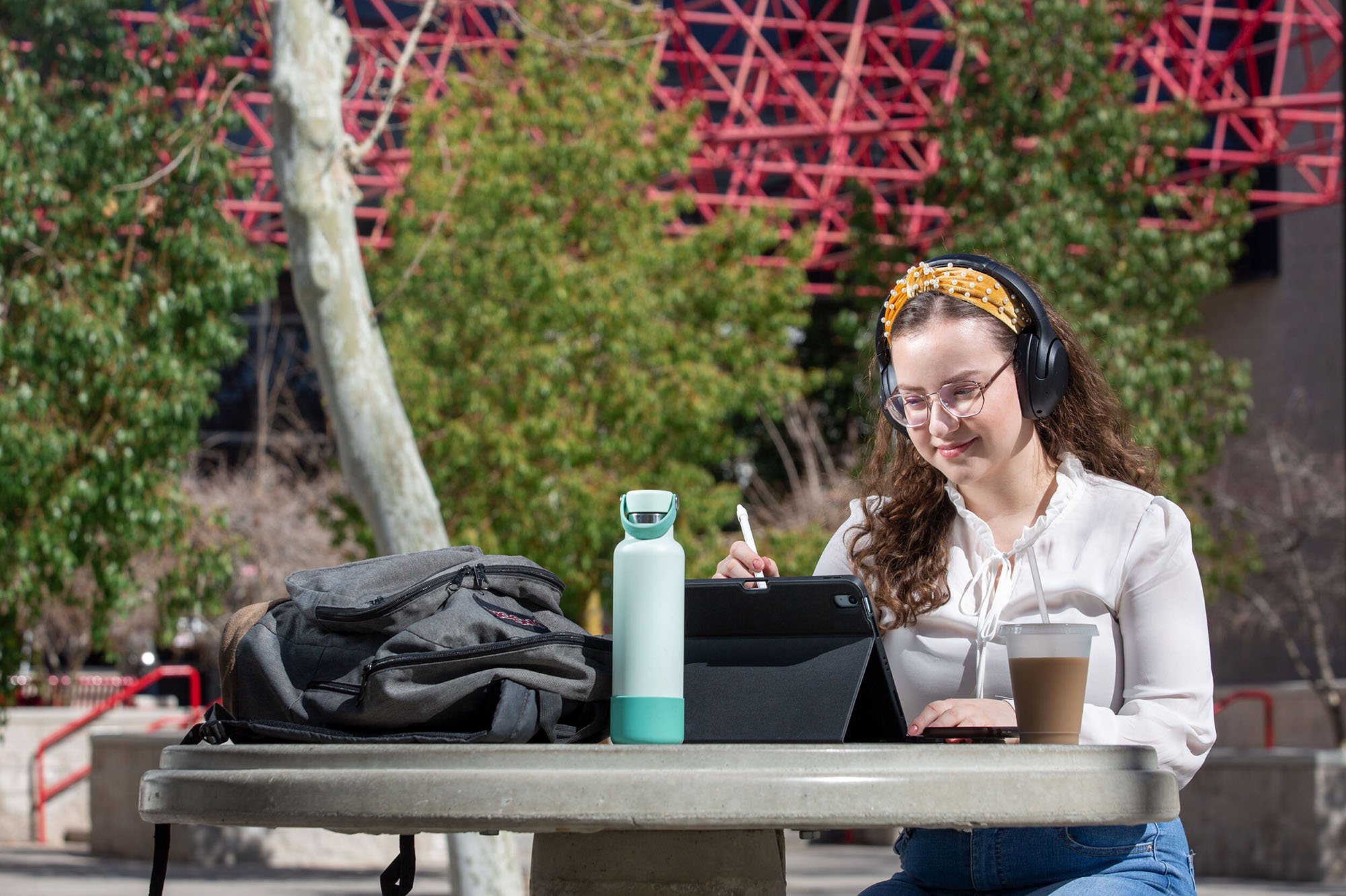 A student sits outside looking down at a tablet