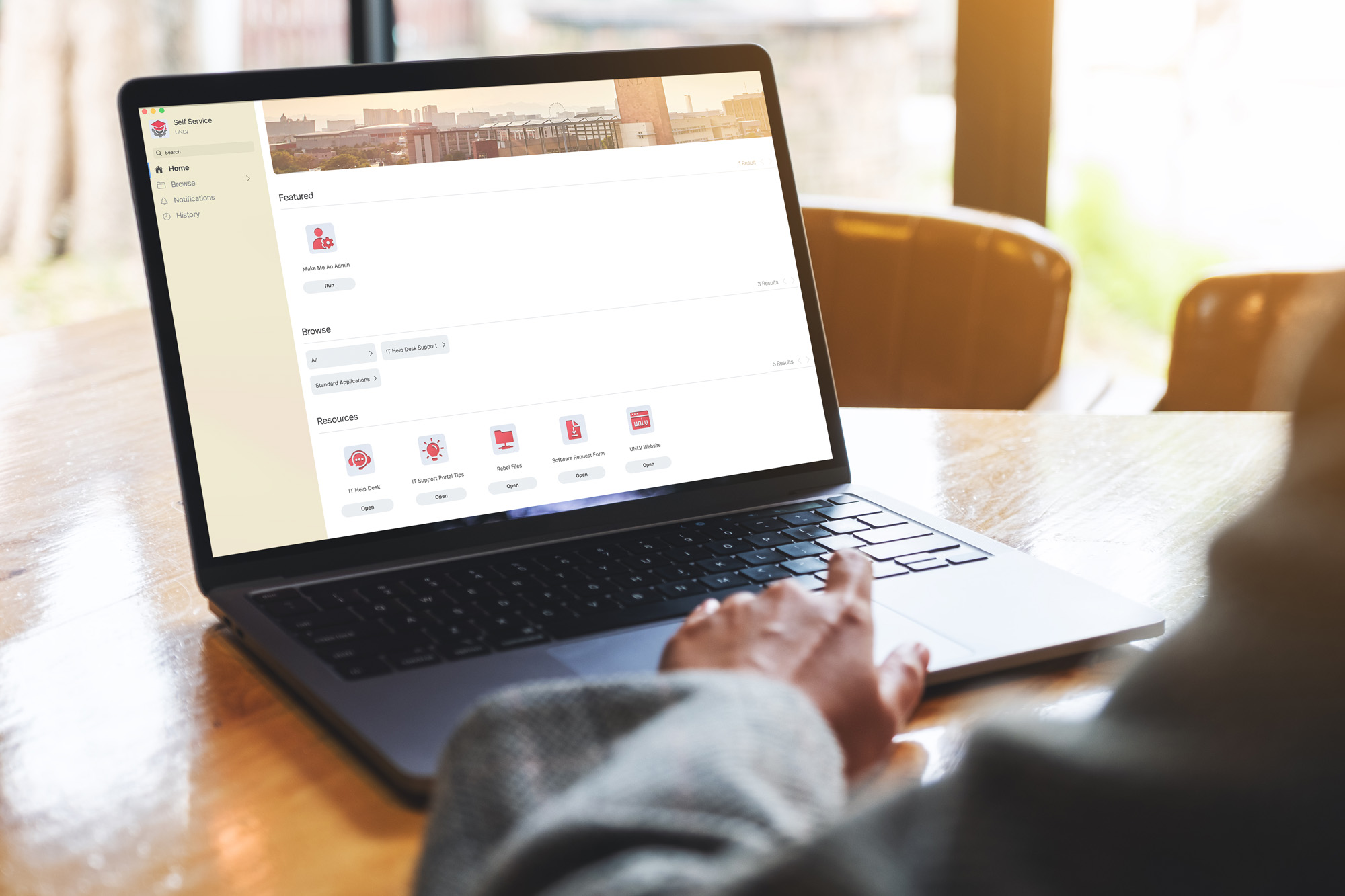 A person scrolls an open laptop with the UNLV self-service portal visible.