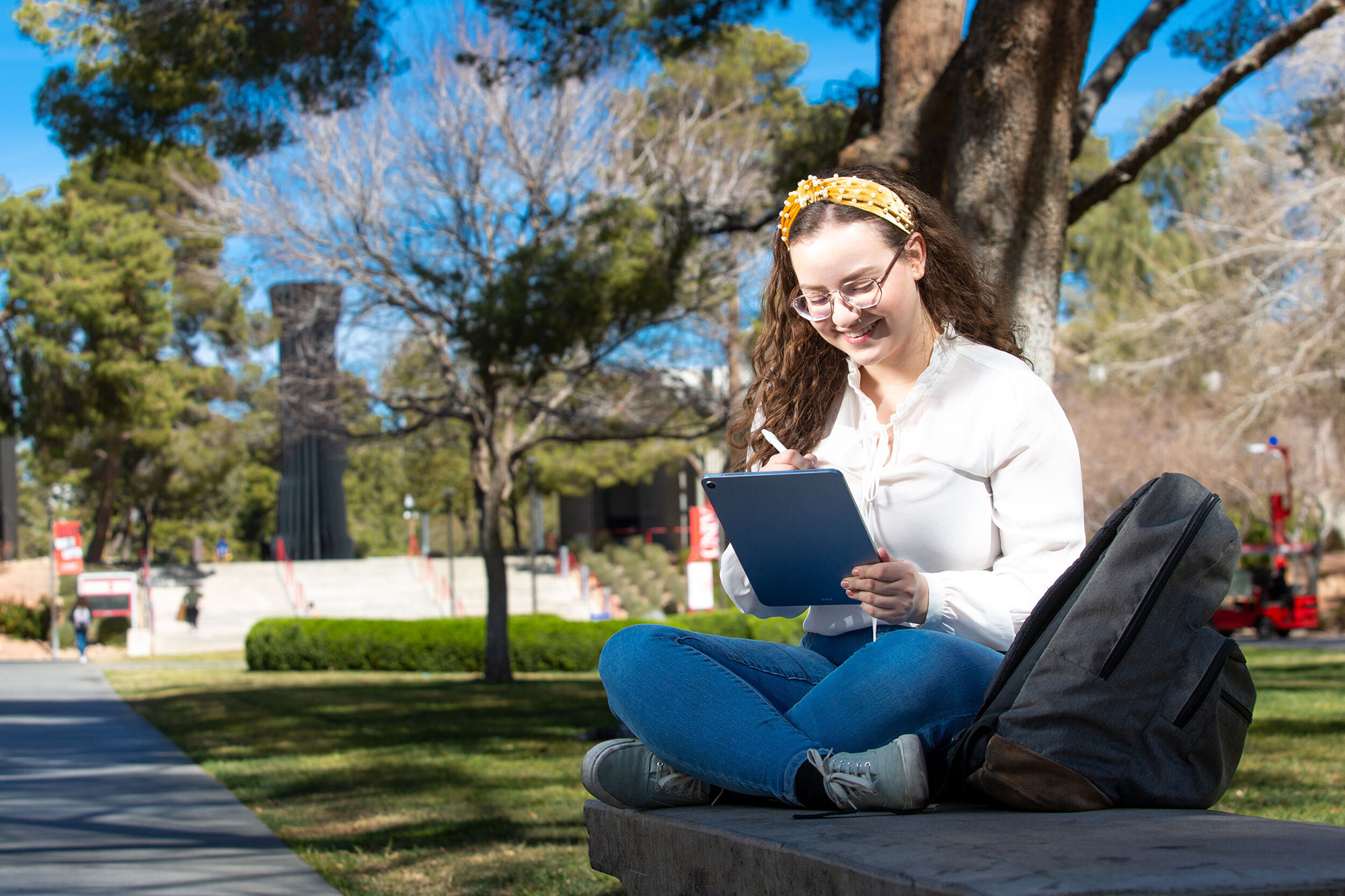 A student sits outside looking down at a tablet