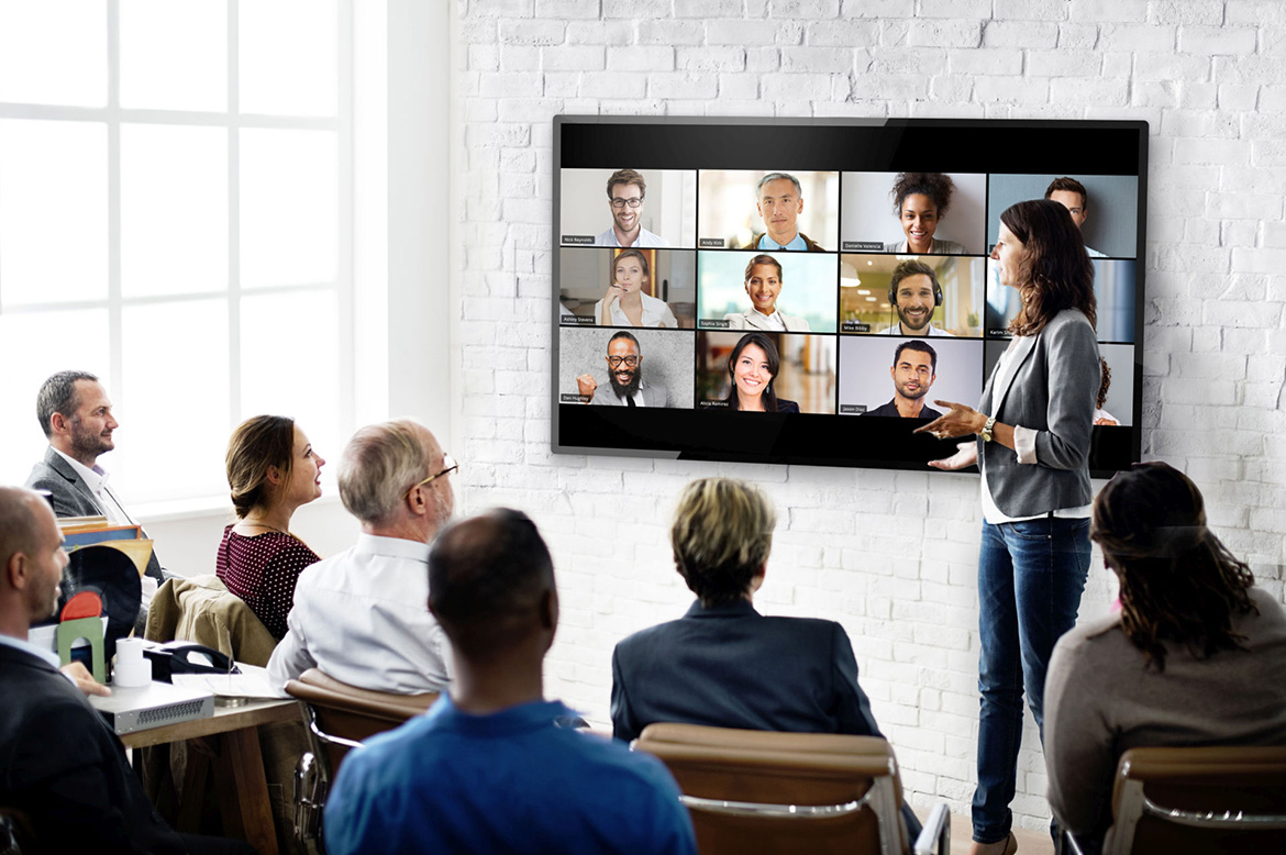 A group of people peer up at a Zoom conference on a large monitor.