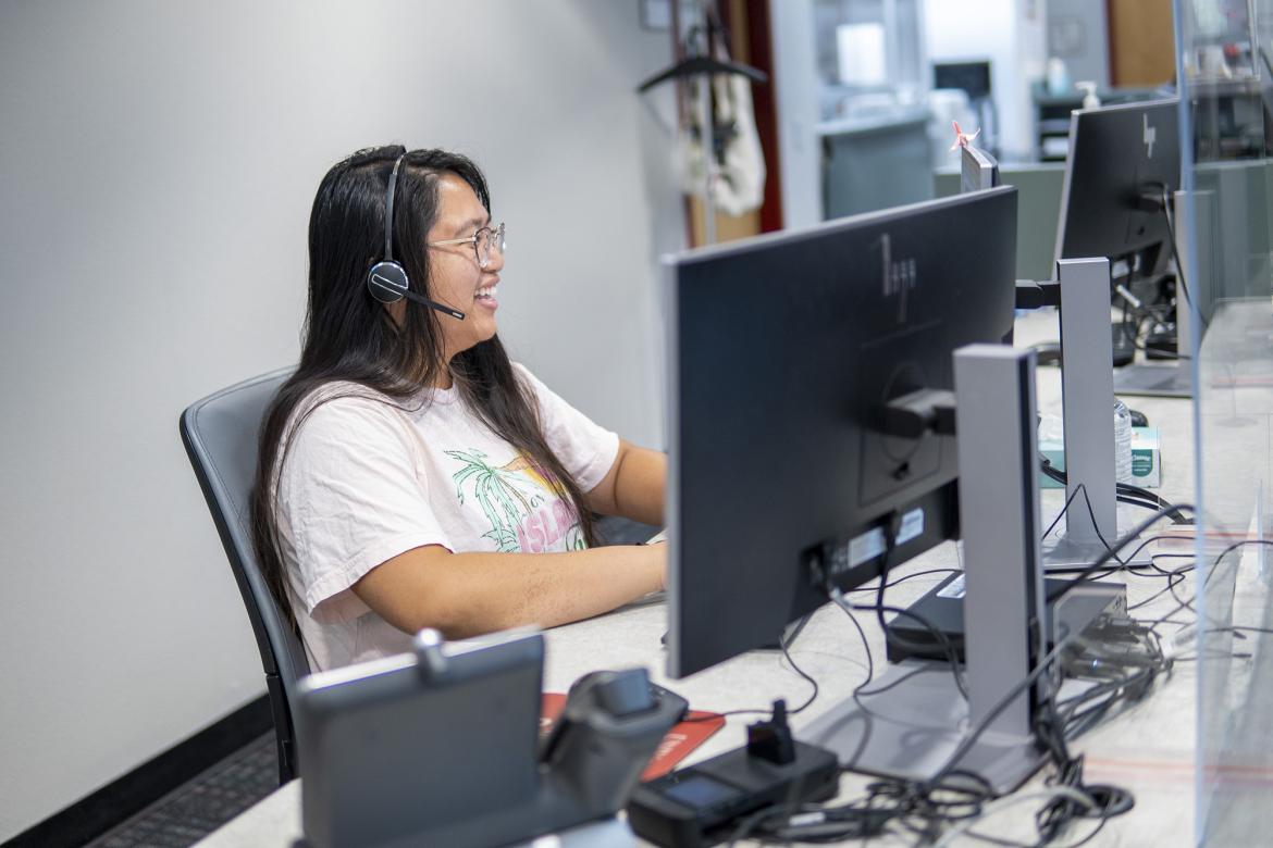 A smiling student wearing a headset works the IT Help Desk.