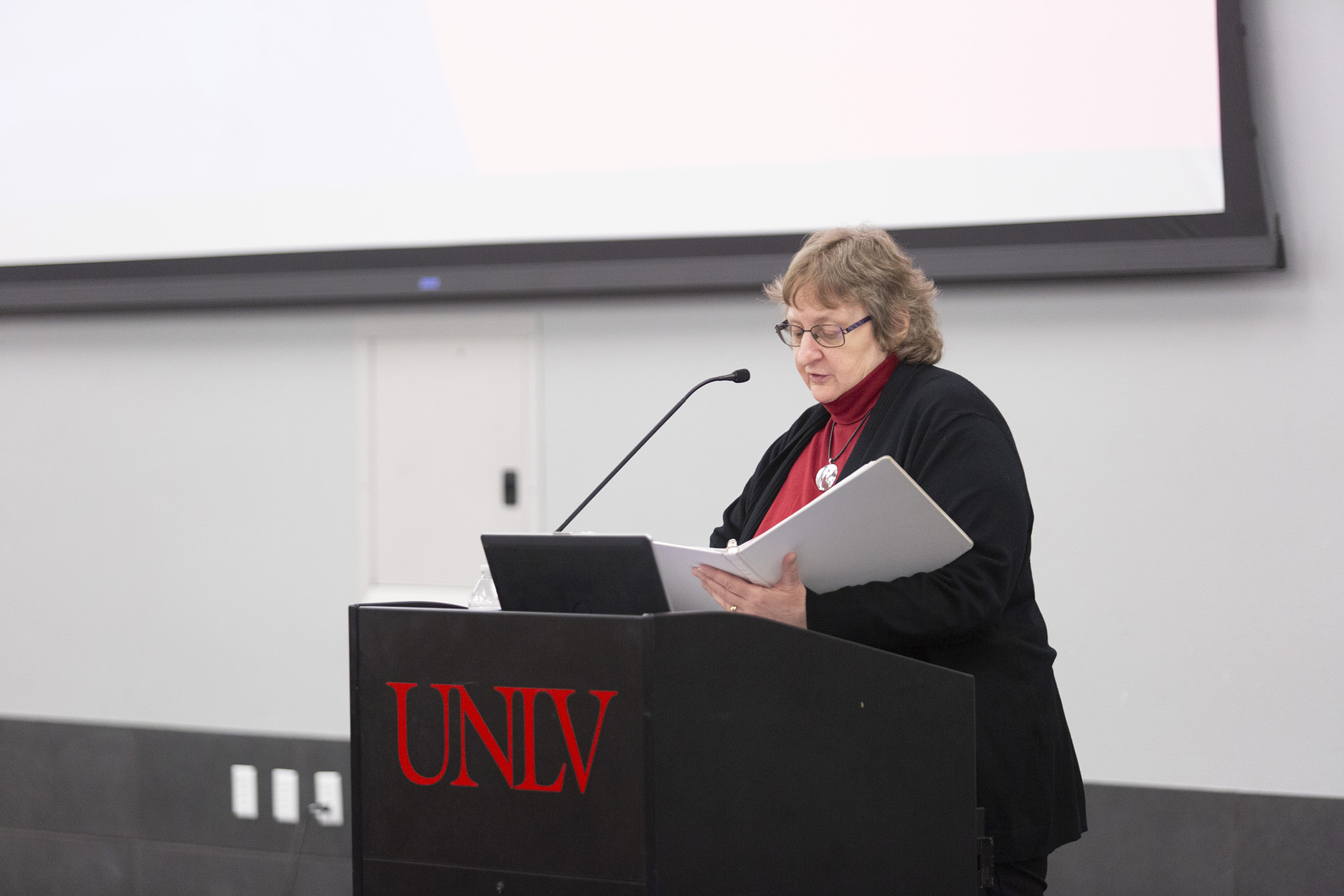 Dr. Lori Temple stands at a lectern looking down at her notes.