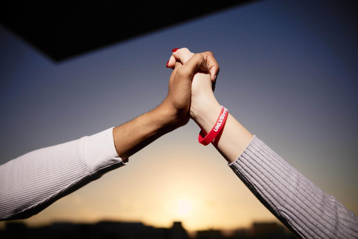 Close shot of two clasped hands, one with a red Rebel Strong bracelet.