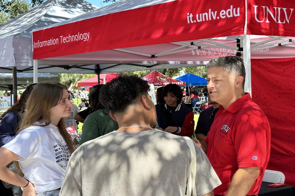 Person talking to two people near a tent that says information technology