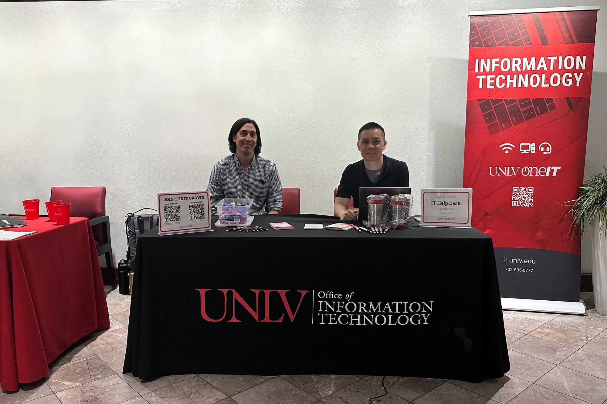 Two people sitting at table with cloth that reads UNLV Office of Information Technology