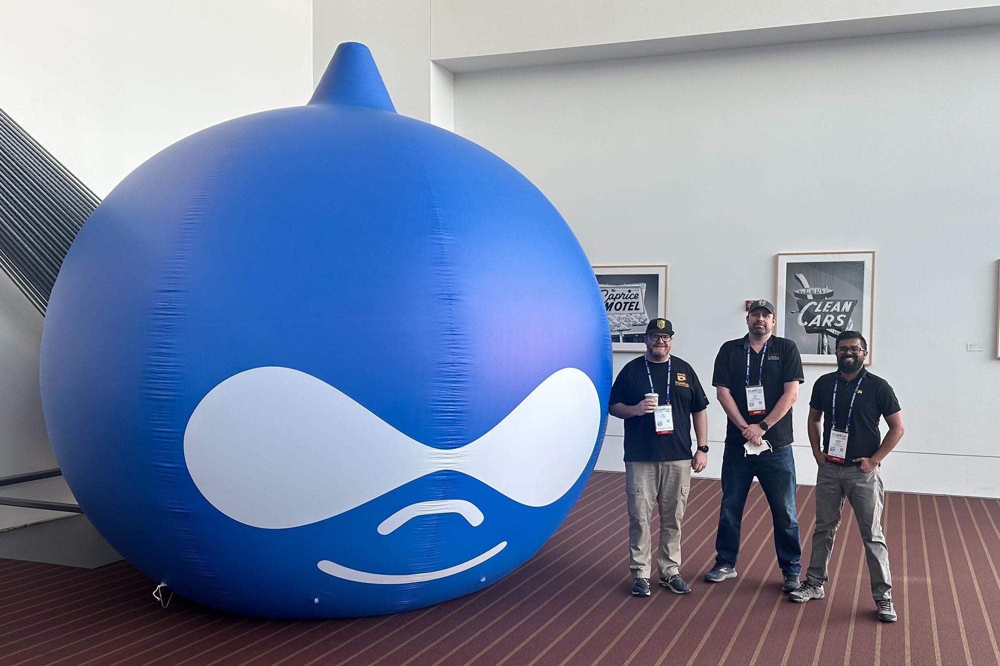 Group of people standing next to a large, blue inflatable water drop, the Drupalicon.