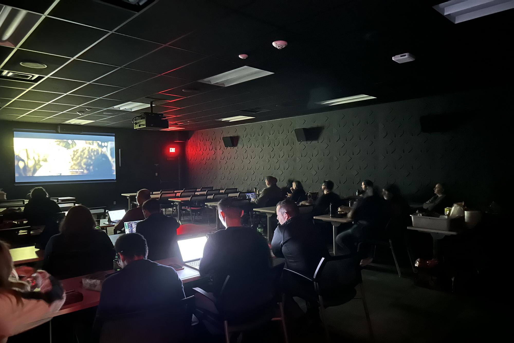 People sitting in classroom looking a projection screen at front of room