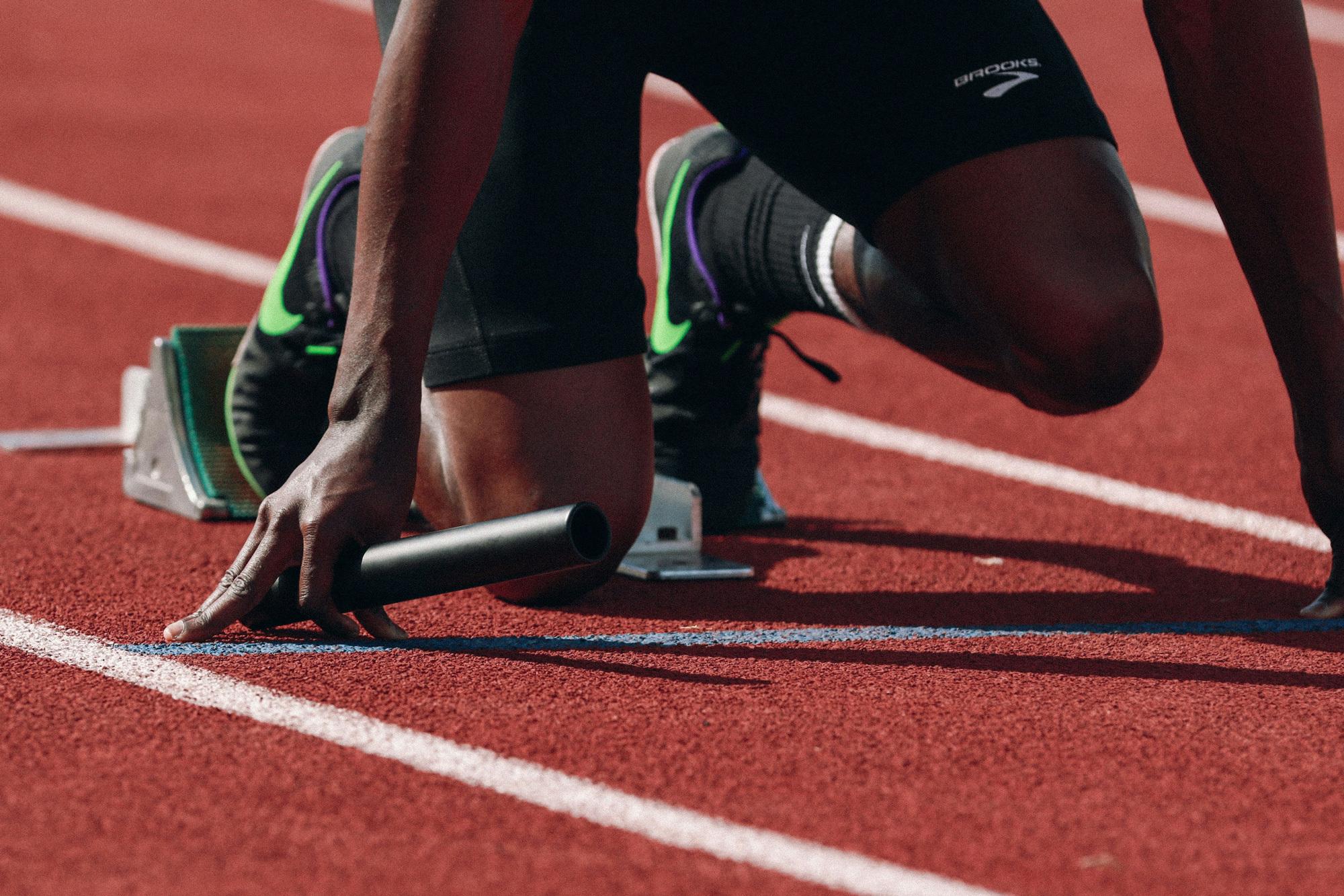 Person squatting for race on a track with baton in hand.