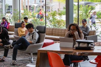 Group of people sitting in chairs or at a desk looking at their laptops and phones.