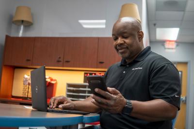 Person holding mobile device in one hand, typing on a laptop computer with other hand