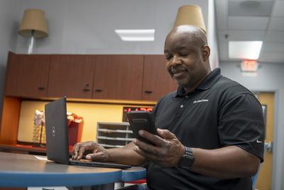 Person holding a smartphone in one hand and typing on a laptop computer with the other hand