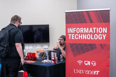 Person sitting down talking to another person with red Information Technology sign on the side