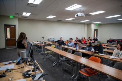 Group of people in classroom listening to person speaking.