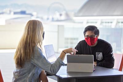 Two people wearing a face covering, sitting down, using laptops