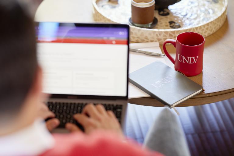 Person typing on laptop computer with UNLV notepad and coffee mug nearby