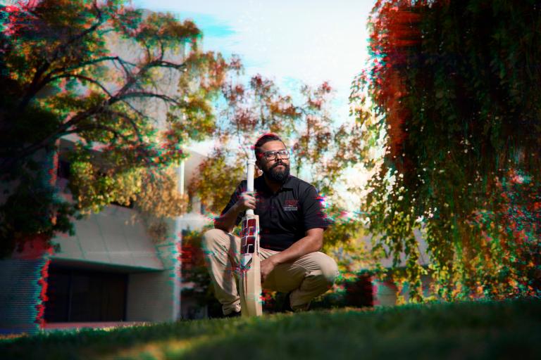 Man holding cricket bat on grass area. 