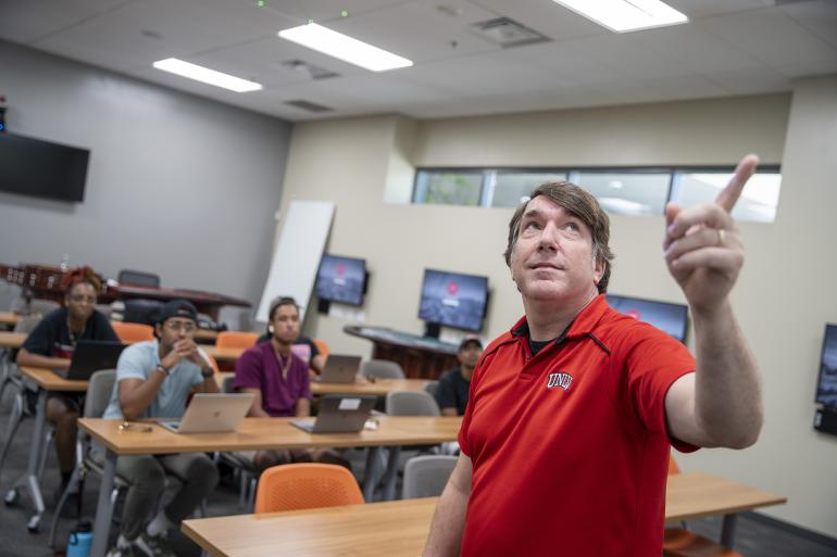 Person pointing to projector in a classroom. 